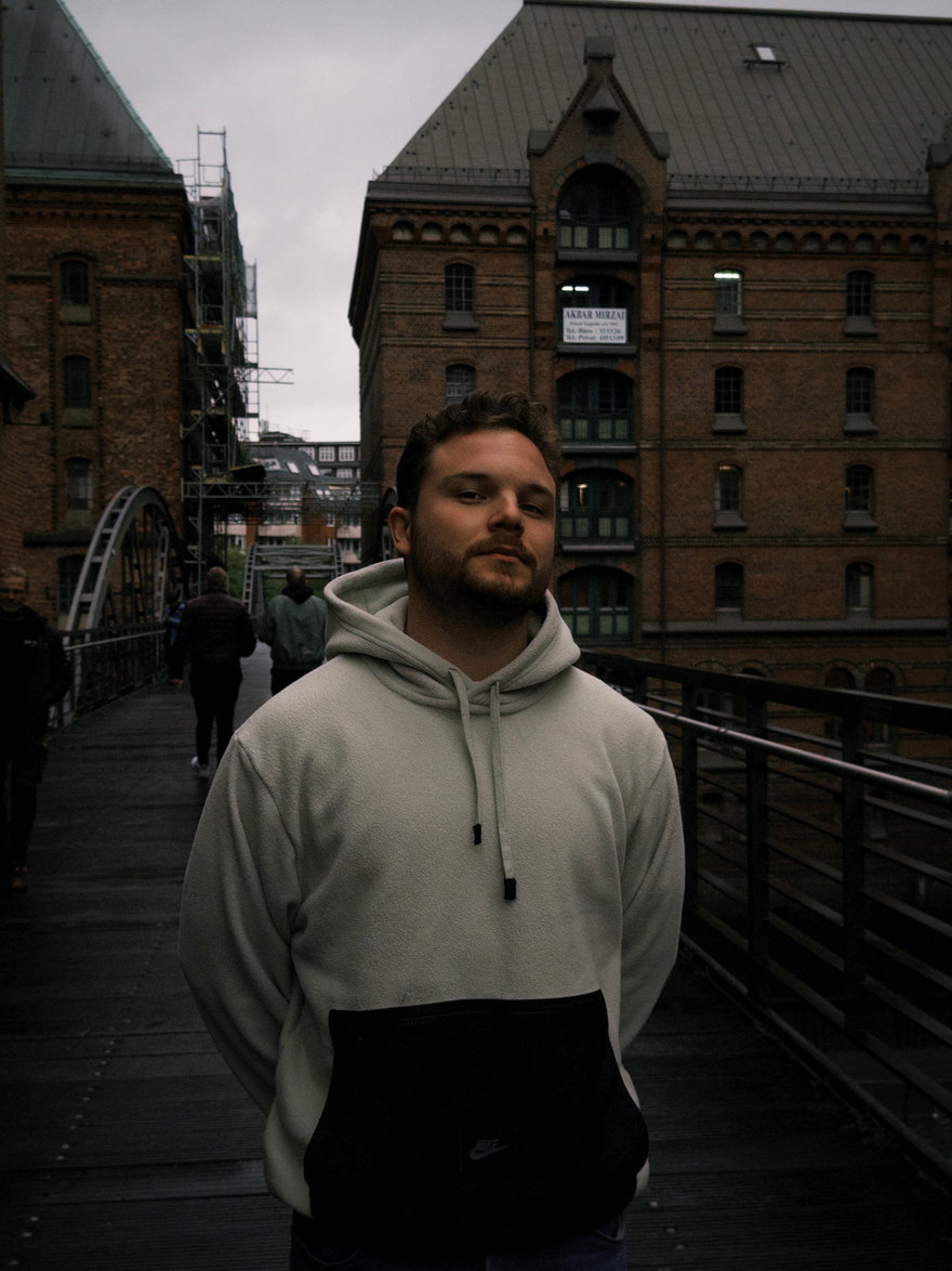 Tufan on a bridge in Hamburg's Speicherstadt, red-brick warehouses behind him.